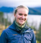 dame med blå jakke står foran en skog