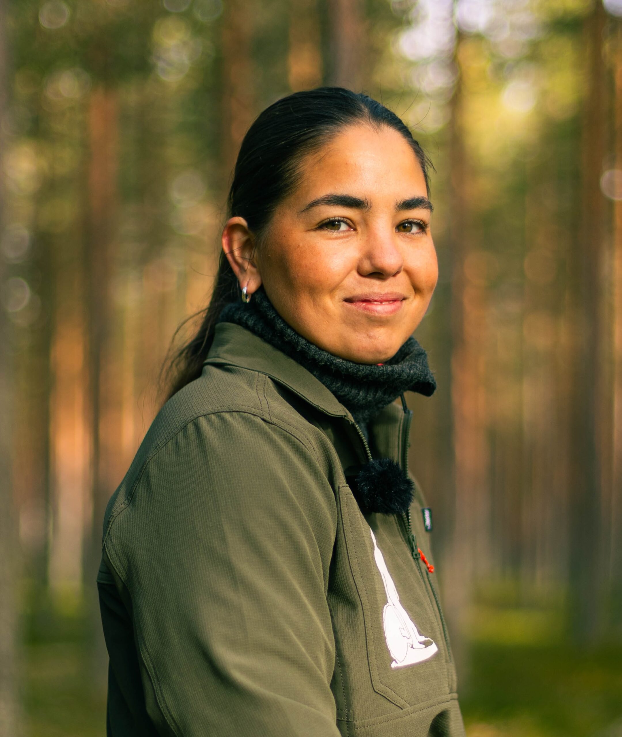 jente med mørkt hår og grønn jakke i en skog