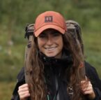 dame ute i skogen med brunt hår og oransje caps med sekk på