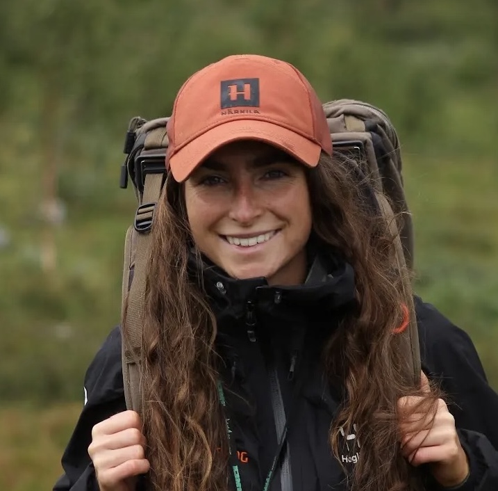 dame ute i skogen med brunt hår og oransje caps med sekk på